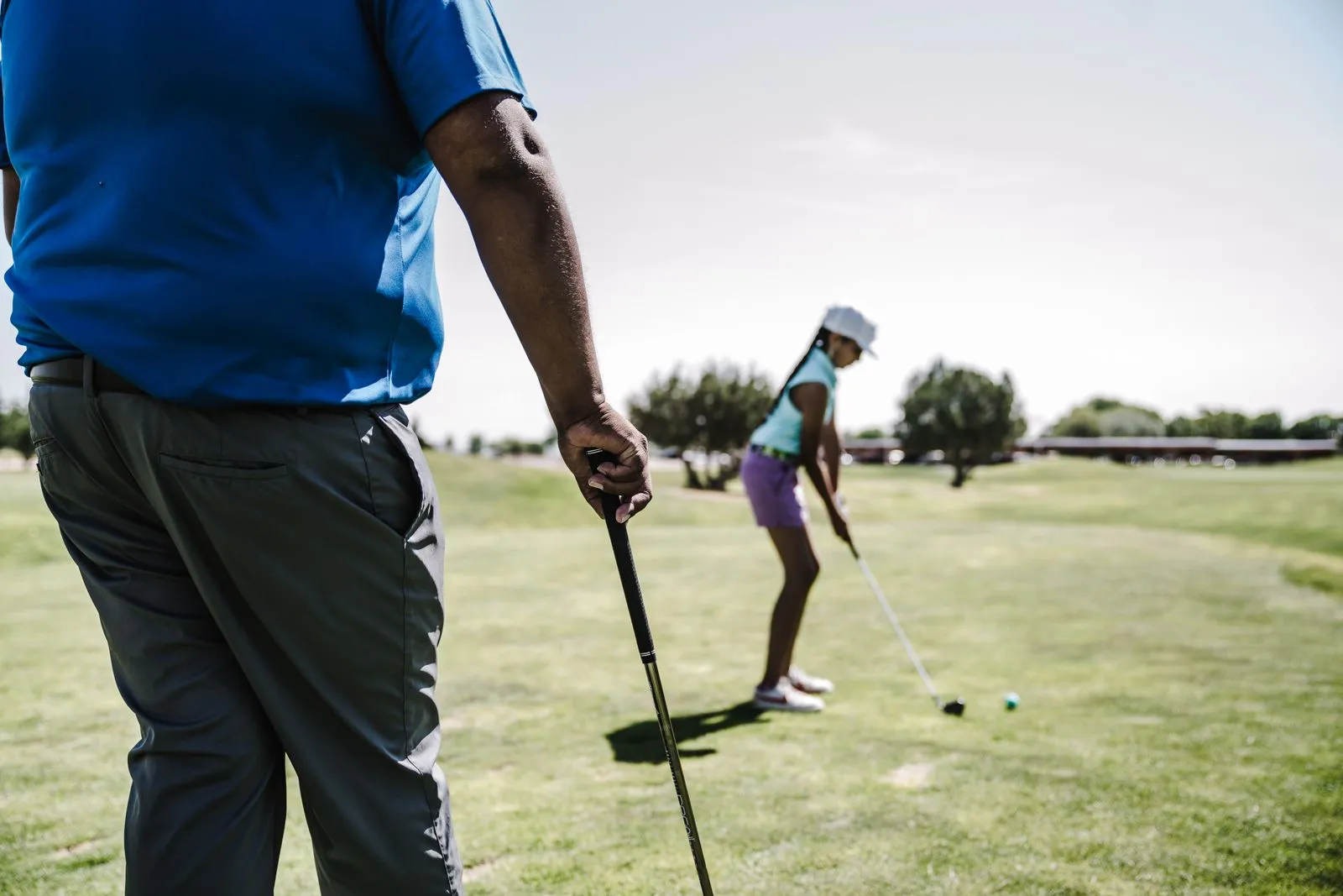 A father and daughter playing golf on a sunny day at a golf course, focusing on putting skills.